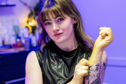 Untitled design (12) Image of local esthetician Taylor D. in her treatment room putting on gold rubber gloves