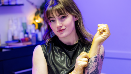 Image of local esthetician Taylor D. in her treatment room putting on gold rubber gloves