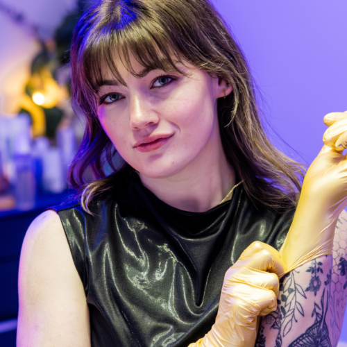 Image of local esthetician Taylor D. in her treatment room putting on gold rubber gloves